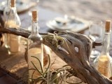 a burlap table runner with driftwood, air plants, bottles and simple glasses and porcelain for a neutral and natural beach tablescape