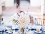 a blue tablecloth, a seashell with blooms and a pastel bloom centerpiece in a glass vase for a beach tablescape