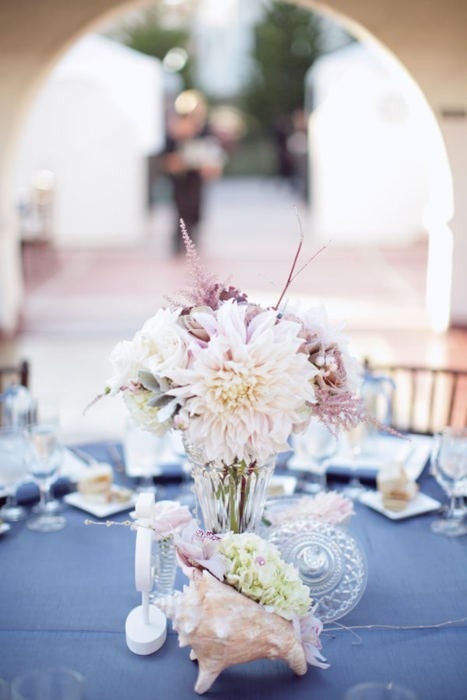 a blue tablecloth, a seashell with blooms and a pastel bloom centerpiece in a glass vase for a beach tablescape