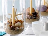 a beach tablescape with large glasses filled with sand, seashells and starfish, candles and blue plates and napkins