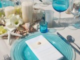 a beach wedding table with candles, white blooms and starfish, blue glasses, glass plates and candleholders