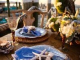 a bright beach tablescape with woven placemats, blue fish plates, blue napkins with starfish napkin rings plus a large neutral bloom centerpiece