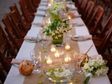 a chic tropical wedding table with a neutral table runner, white blooms and greenery, candles plus floating flowers
