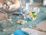 a light blue wedding tablescape with a blue runner and napkins, a jar with sand and seashells, starfish napkin rings and seashells right on the table