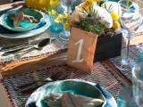 a colorful beach wedding tablescape with woven placemats, blue plates, glasses, a centerpiece with succulents and air plants