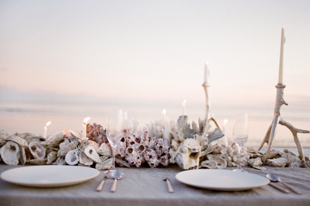 A neutral beach wedding tablescape with lots of corals, seashells, neutral candles and porcelain