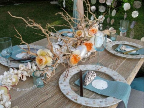 a bold wedding tablescape with pebble printed plates, blue napkins, a seashell and bright bloom centerpiece and driftwood