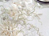 an all-white beach wedding table with corals, driftwood, seashells in a glass globe and dark plates