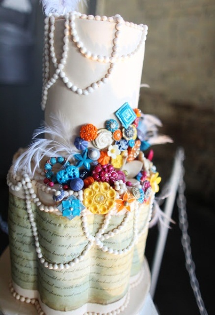 a catchy wedding cake with a white and love letter tier, edible pearls and feathers and lots of colorful beads, brooches and decor for a vintage wedding