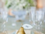 a pretty wedding place setting with a pale blue napkin, a geometric plate and a gilded pear that holds a name