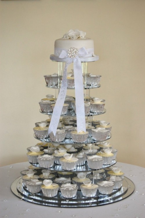a white wedding cake and matching cupcakes in silver liners plus a large bow with rhinestones