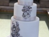 a white winter wedding cake decorated with silver edible elements and a large white bloom on top