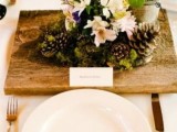 a wedding centerpiece of a board with moss, blooms, pinecones, a bucket with greenery is very whimsy and creative