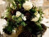 a lush winter wedding centerpiece of white blooms, ferns, twigs, pinecones placed into a tree stump looks wow