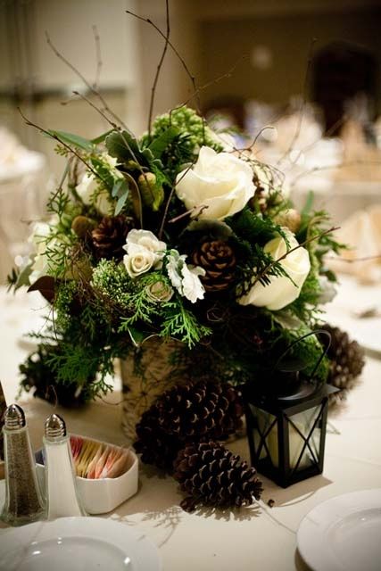 a lush winter wedding centerpiece of white blooms, ferns, twigs, pinecones placed into a tree stump looks wow