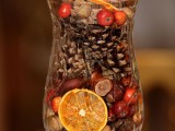a tall glass with berries, pinecones, dried citrus, nuts and wood is a lovely wedding centerpiece