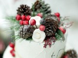 a white textural wedding cake with berries, pinecones, white blooms and greenery is a lovely winter-inspired wedding dessert