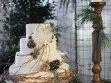 a white wedding cake with pinecones, feathers and twigs plus candles around is a lovely idea for a winter wedding
