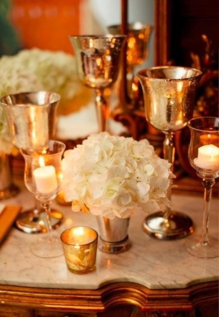 a lovely gold and white wedding centerpiece with gilded glasses, white blooms and candles is a cool idea for a wedding