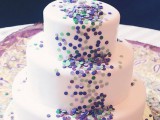 a white wedding cake covered with colorful confetti and with a glass with confetti as a topper is all fun