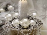 a silver wedding centerpiece of a bowl with silver ornaments and beads and a silver candle in the center is an easy and pretty idea