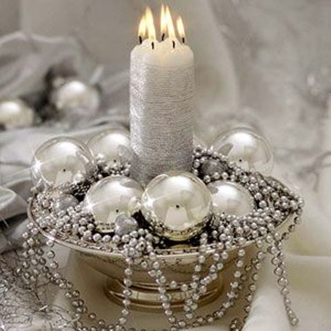 a silver wedding centerpiece of a bowl with silver ornaments and beads and a silver candle in the center is an easy and pretty idea