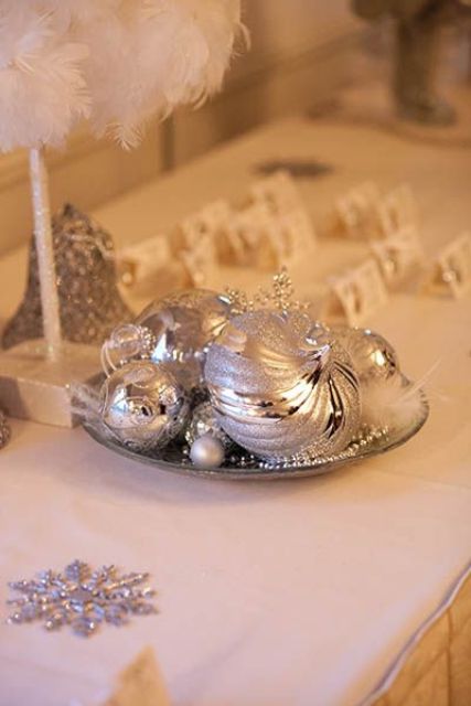 a plate with silver Christmas ornaments and feathers is a lovely decoration for a winter or holiday wedding