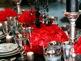 a refined Halloween wedding tablescape with a black glitter tablecloth, bright red blooms, chic glasses and candleholders and printed plates