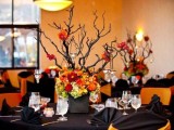 a bold black and orange Halloween wedding tablescape with black napkins, branches in a planter and bold blooms at the base