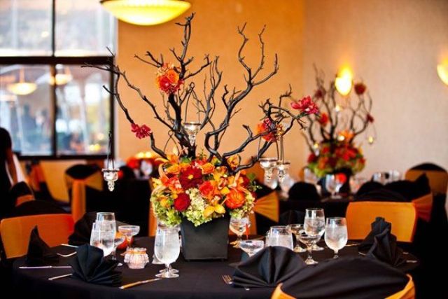 A bold black and orange Halloween wedding tablescape with black napkins, branches in a planter and bold blooms at the base