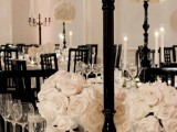 a sophisticated black and white Halloween wedding tablescape with black candleholders and large white rose topiaries, stylish tableware and linens