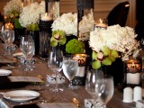 a refined Halloween wedding tablescape with green and white blooms, black lace covering candleholders and vases, neutral plates and a silver tablecloth