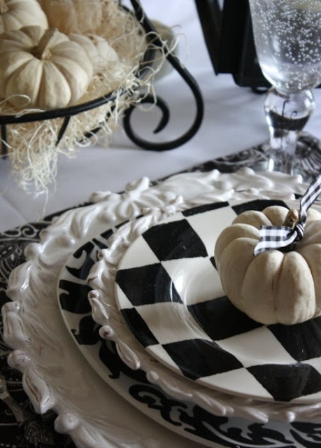 a rustic black and white Halloween table setting with printed plates, white pumpkins, a hay centerpiece