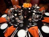 an elegant black, orange and white Halloween wedding tablescape with orange napkins and bold blooms and candles
