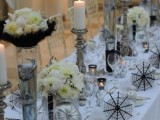 a white, silver and black Halloween wedding tablescape with lush white blooms and feathers, spiderwebs, candles and silver pumpkins