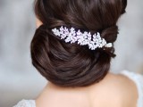 an elegant and sleek low updo with side parting, a volume on top and a large botanical rhinestone hairpiece to accent the hairstyle