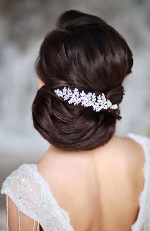 an elegant and sleek low updo with side parting, a volume on top and a large botanical rhinestone hairpiece to accent the hairstyle