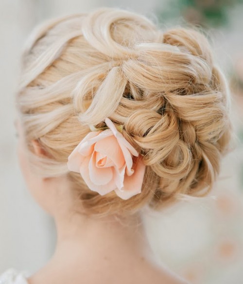 a wavy updo with much volume and some curls accented with a single peachy bloom is a chic idea for a spring or summer bride