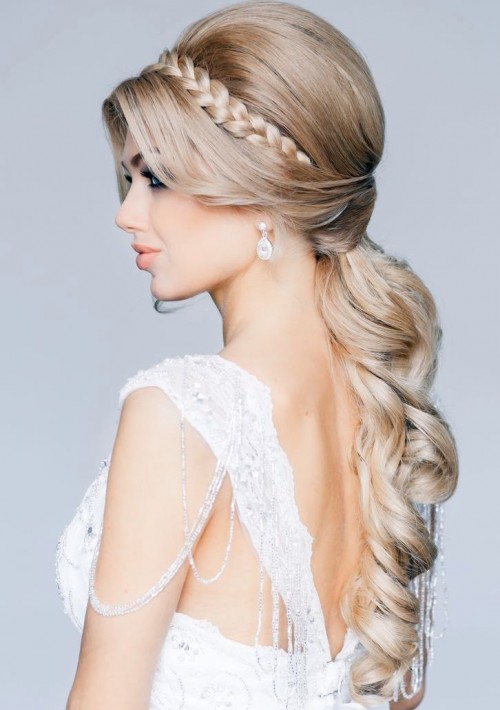 a long wavy ponytail with a volume on top and a braided halo is a lovely and elegant wedding hairstyle for a formal bridal look with a touch of modern
