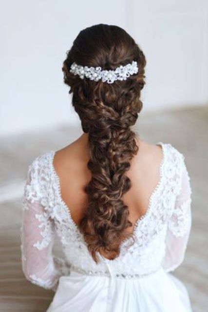 a long wavy and braided ponytail with a bit of curls on the ends and a refined rhinestone hairpiece that accents the hairstyle is amazing
