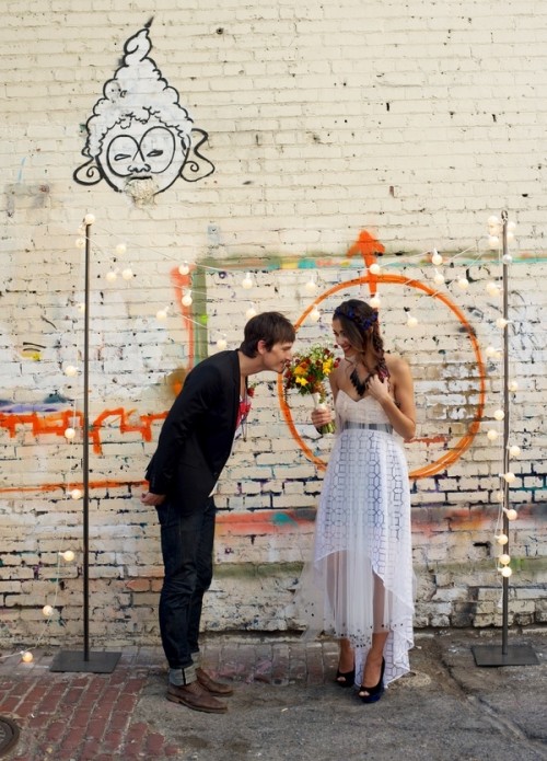 a graffiti wall as a wedding backdrop plus a simple wedding arch with lights, an orange wreath for bold wedding looks