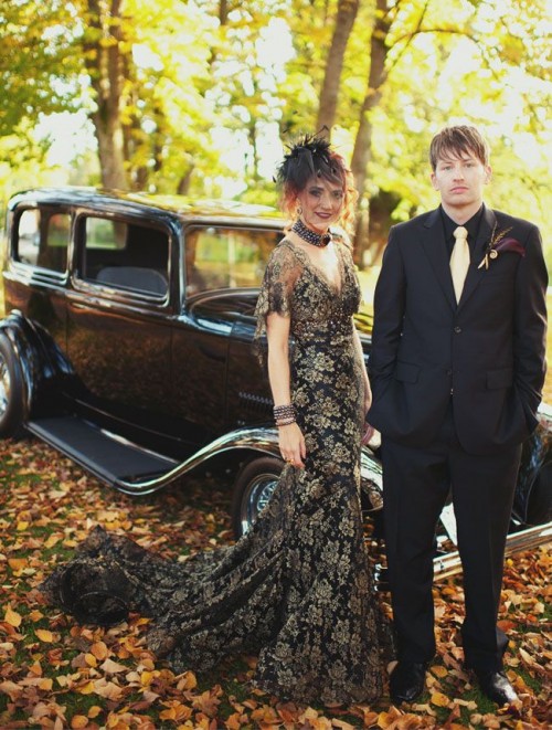 a black and gold lace mermaid wedding dress with a V-neckline, short sleeves, a train and a feather headpiece with a veil