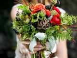 a bright woodland boho wedding bouquet of fern, greenery, berries, bright blooms, feathers, and lotus pieces