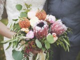 a pretty woodland-inspired wedding bouquet of pink proteas, red pincushion ones, white blooms, berries and various greenery