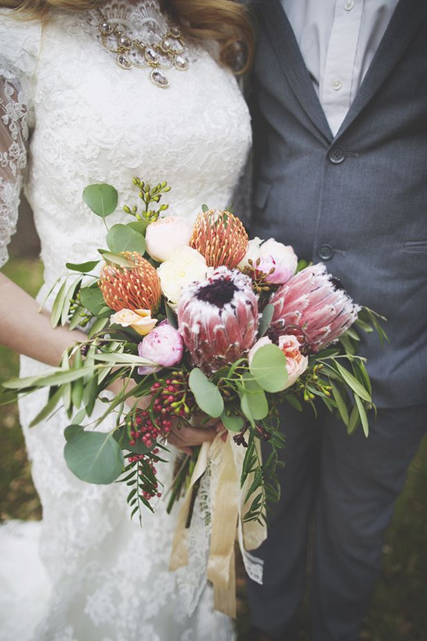 A pretty woodland inspired wedding bouquet of pink proteas, red pincushion ones, white blooms, berries and various greenery