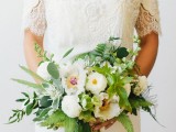 a chic wedding bouquet of various types of greenery and foliage and white blooms plus gold ribbons is wow