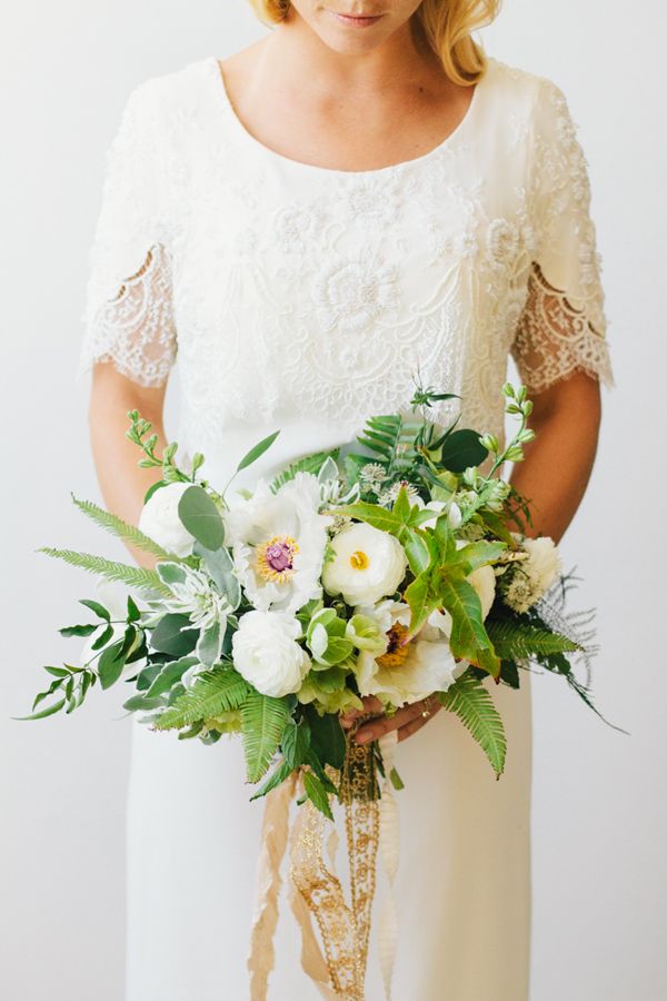 A chic wedding bouquet of various types of greenery and foliage and white blooms plus gold ribbons is wow