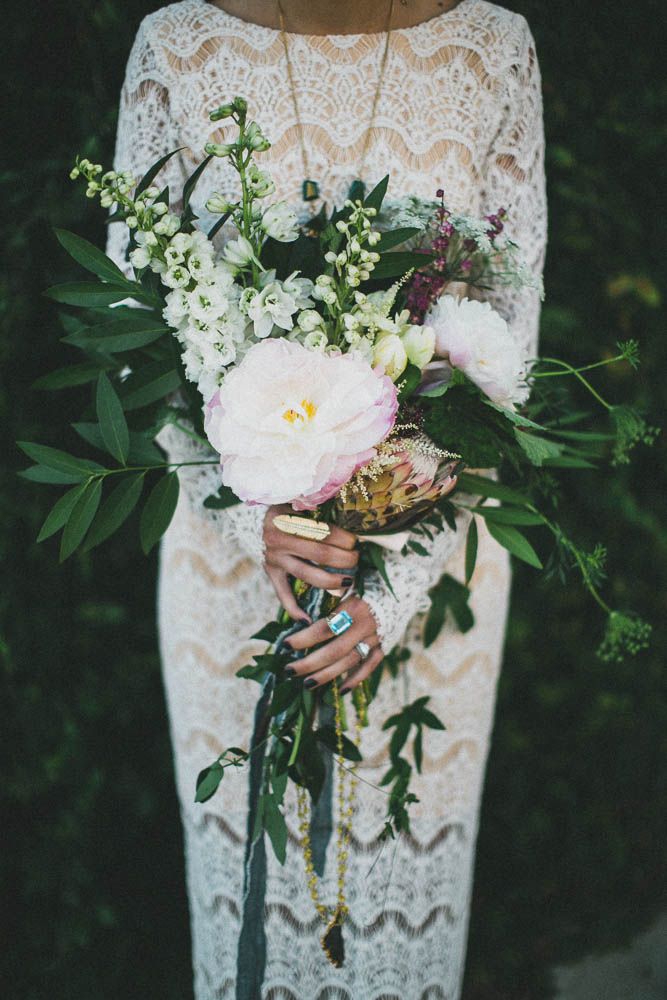 A large and dimensional wedding bouquet with greenery, white and pink blooms, herbs and long gold ribbons with tassels is wow