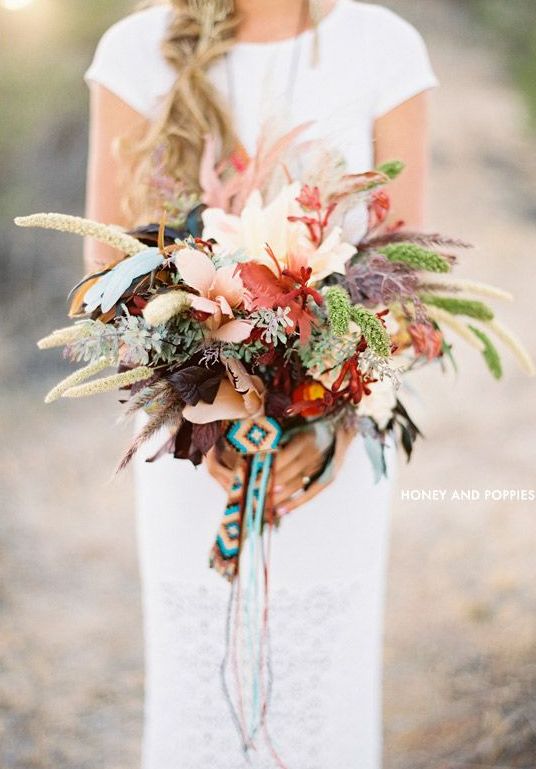A bold boho forest wedding bouquet with various kinds of foliage, dried leaves and feathers and some boho woven ribbons plus no blooms