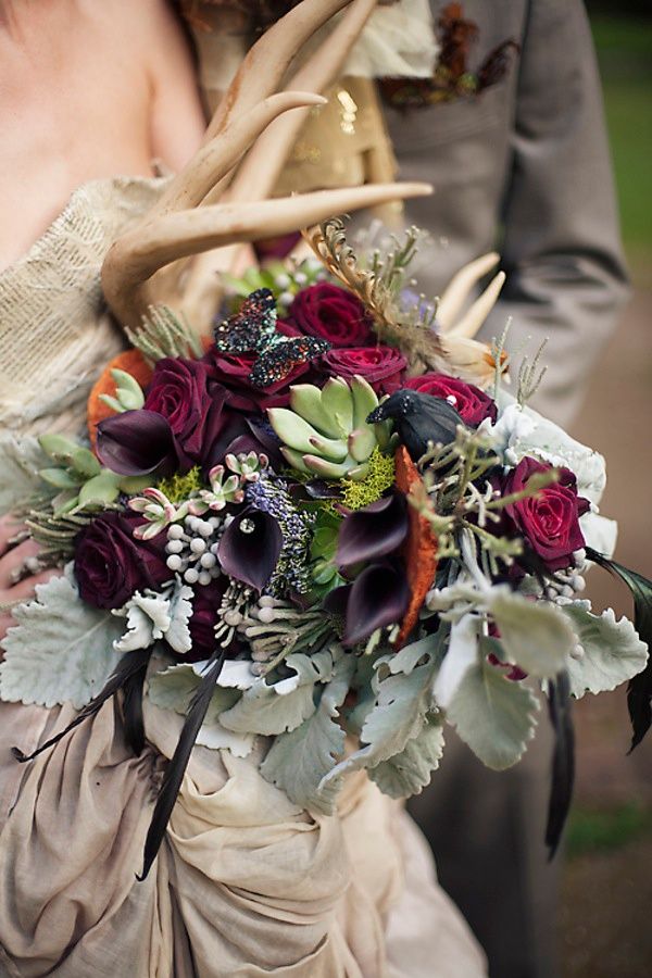 A dark woodland wedding bouquet of deep purple roses and callas, pale greenery, antlers, succulents and antlers for a fall woodland bride